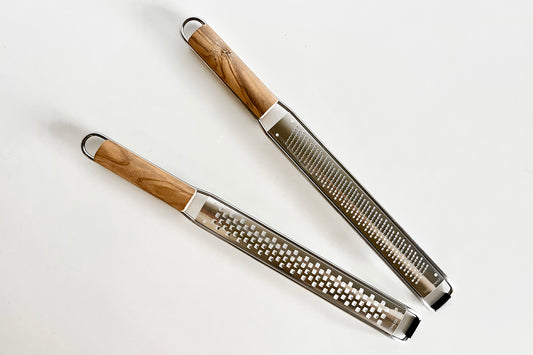 Two stainless steel graters with olivewood handles and metal rings, one with small holes and one with fine ridges.