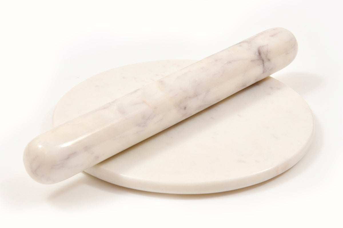 White marble rolling pin resting on round marble board with veined surface.
