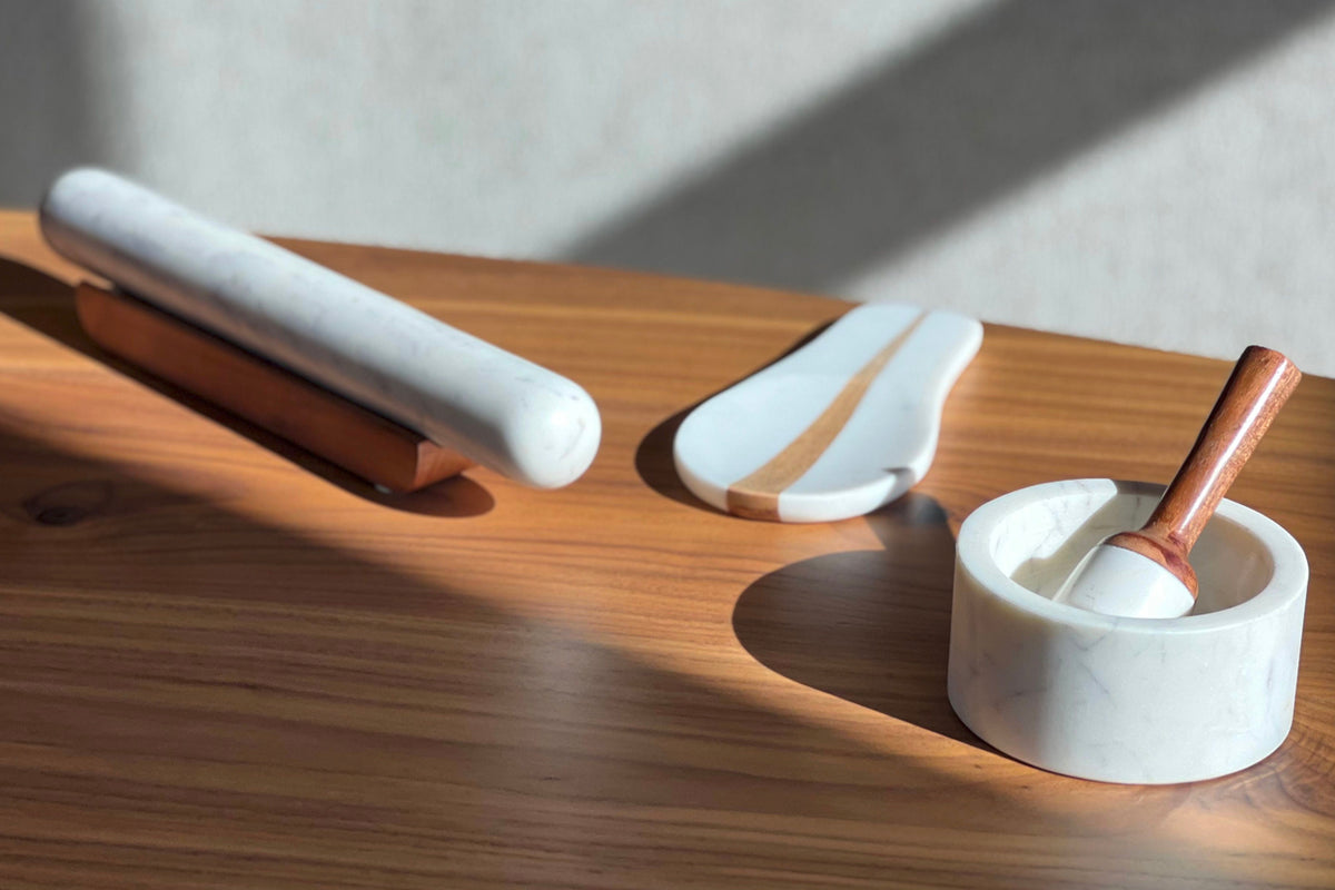 White marble rolling pin and tools on wooden base, including pestle and mortar with copper handle.