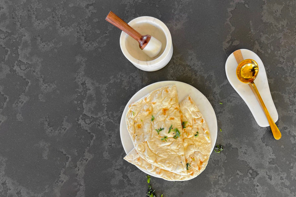White marble spoon rest with wooden handle, shown with cooking utensils and food on dark surface.