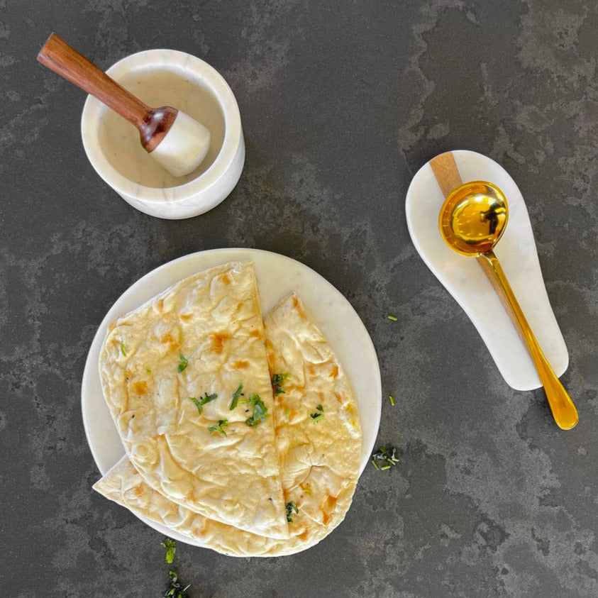 White marble boards with wooden-handled pestle, oil spoon, and butter knife, displayed on dark textured surface.