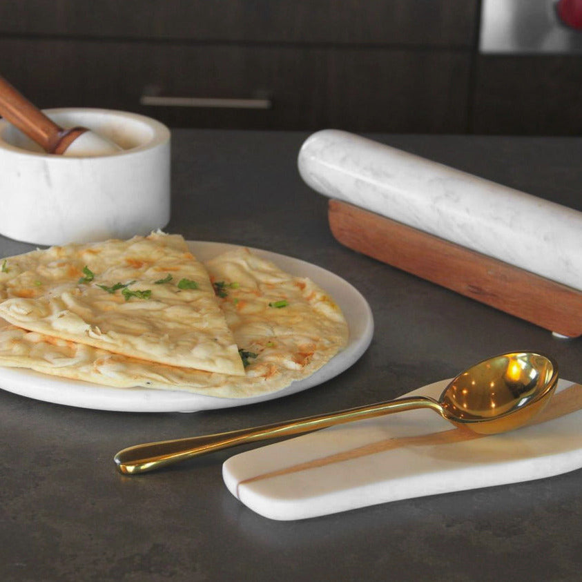 White marble rolling pin and cheese board set with wooden handles displayed with food and gold spoon.