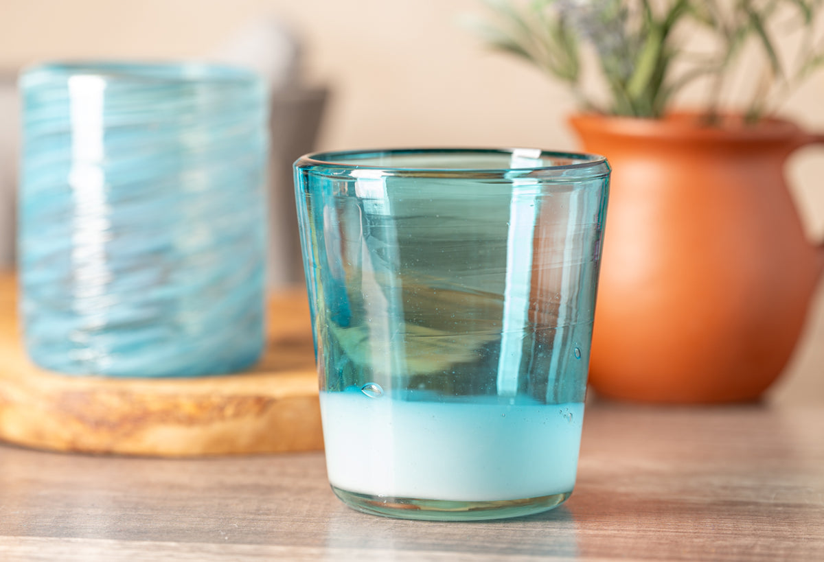 Two turquoise handblown glasses with swirled patterns, one filled with water, displayed on wooden surface.
