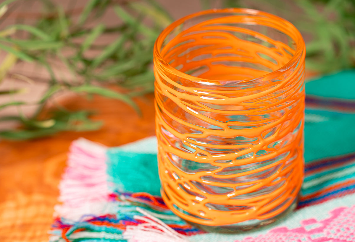 Orange handblown glass with horizontal striped pattern, displayed on colorful woven fabric.