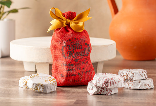 Red mesh gift bag with gold ribbon bow containing wrapped hot chocolate tablets in white and burgundy packaging.