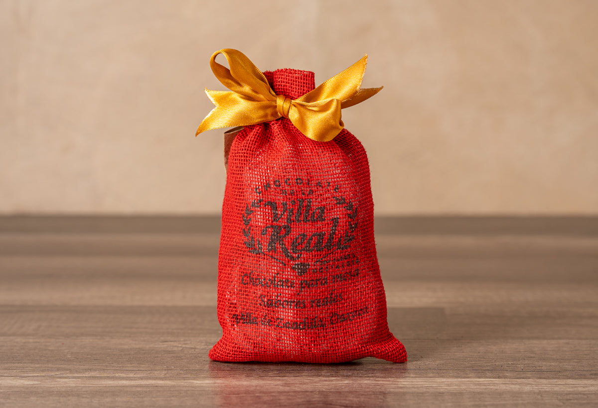 Red burlap bag with gold ribbon bow containing Villa Real Mexican hot chocolate variety set.