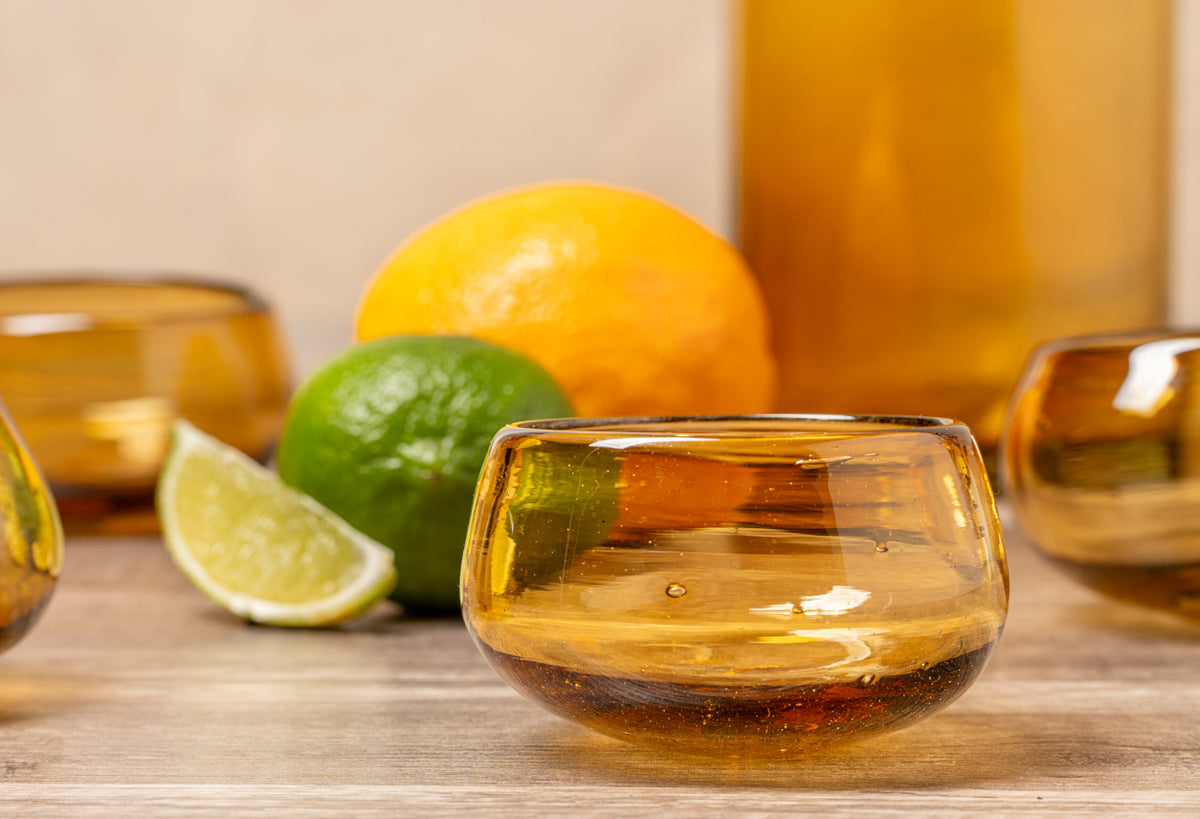 Tasting glasses filled with amber liquid beside fresh limes and lemons on a wooden surface.