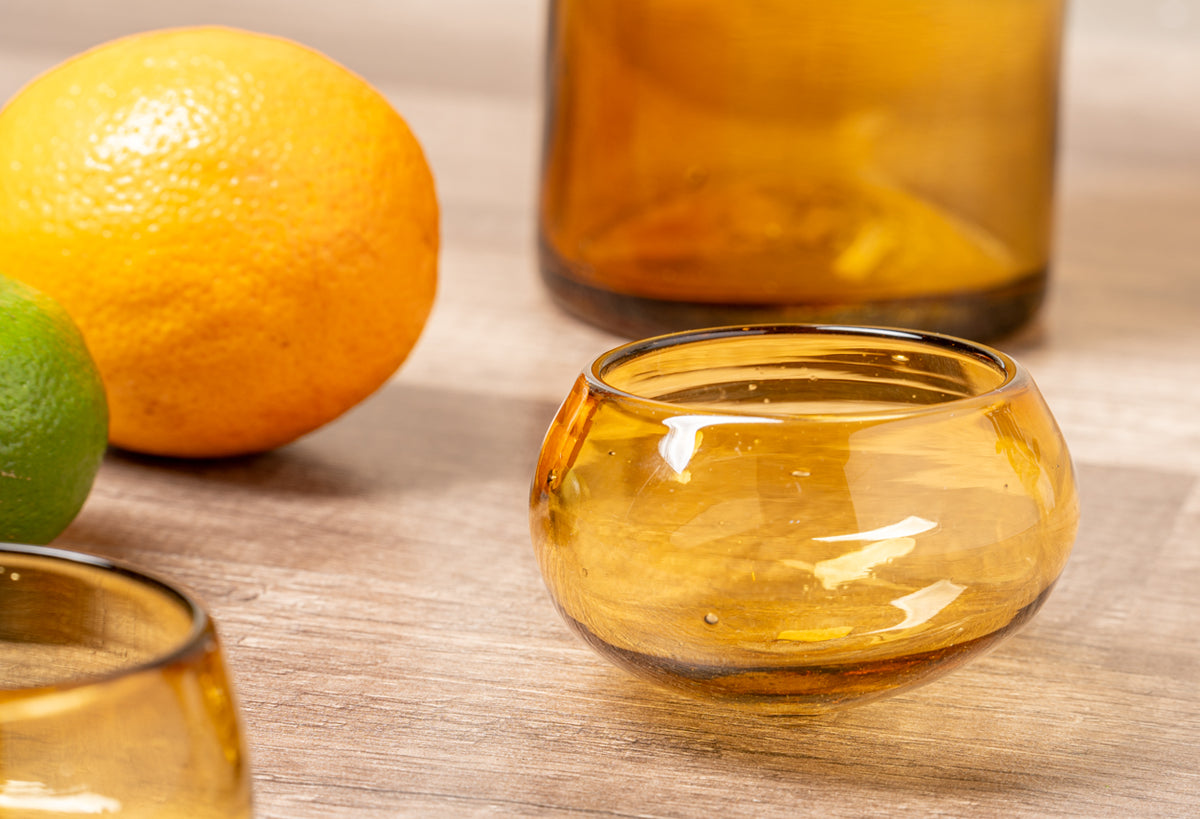 Amber glass tasting glasses and bottles with orange and lime on wooden surface.
