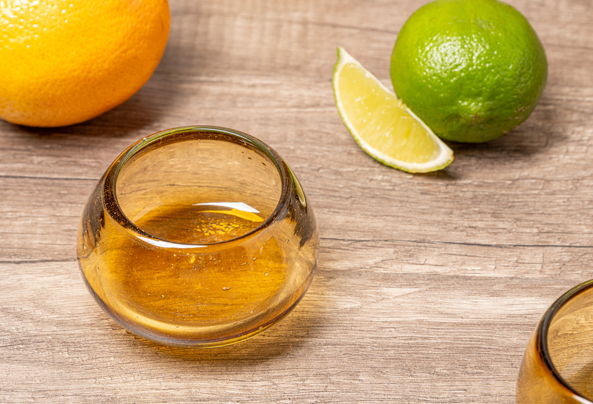 Glass of amber liquid with yellow and green citrus fruits and sliced lime on wooden surface.