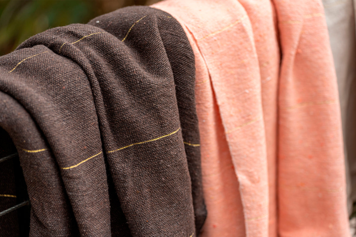 Charcoal gray and coral woven blankets with gold stripe details draped together.