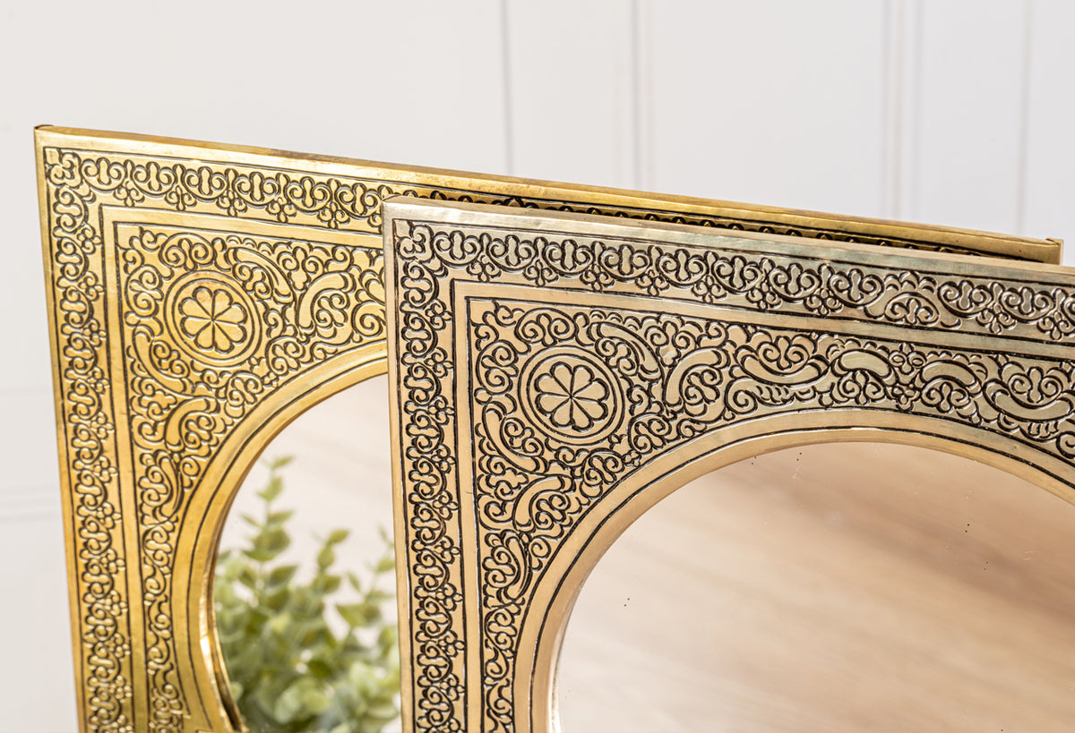 Gold-framed mirror with ornate filigree detailing and arched center design, showing partial reflection of greenery.