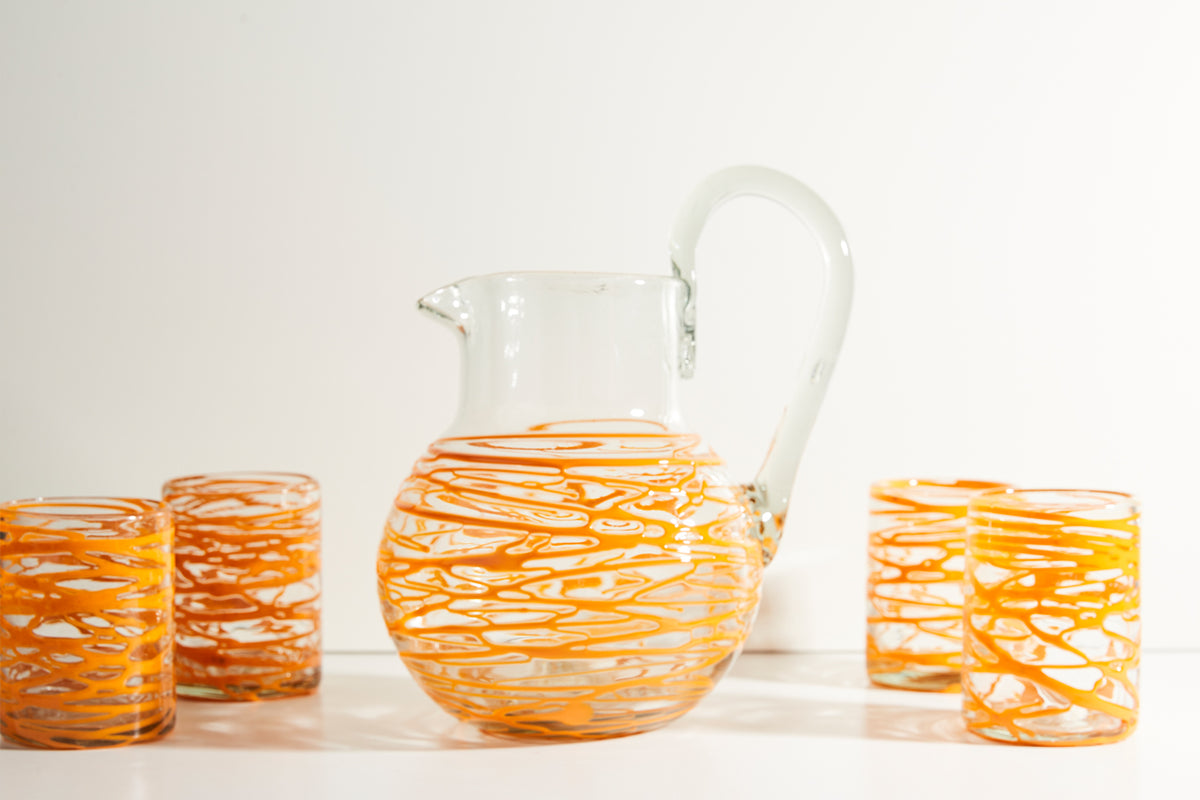 Clear glass pitcher with curved handle and orange linear pattern, displayed with four matching glasses.