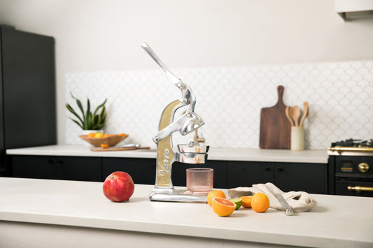 Small citrus juicer with wooden and metal construction, displayed on kitchen counter with lemons and pomegranate.