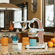 White and coral citrus juicer with fresh oranges and juice glass on granite countertop.