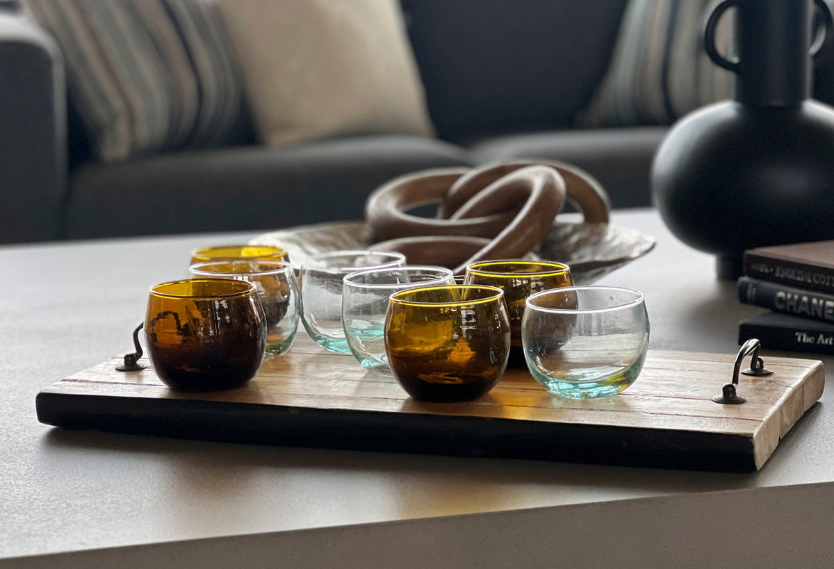 Four stemless goblets with amber and clear glass on wooden serving tray.