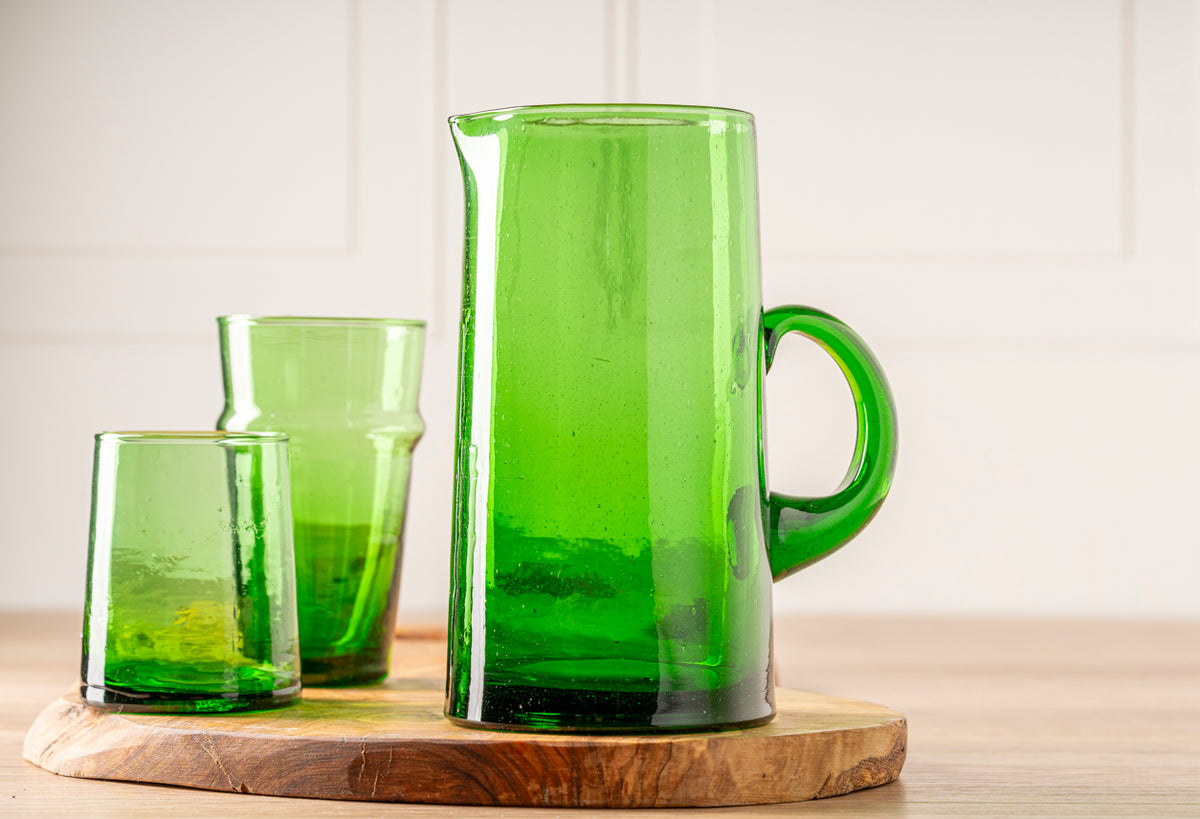 Three green glass jugs of varying sizes with cone shapes, displayed on a wooden base.