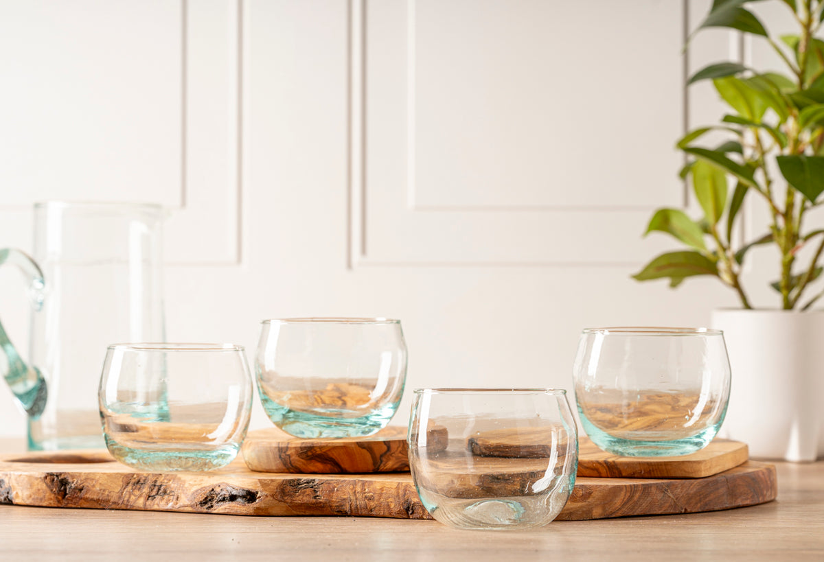 Four clear stemless goblets with turquoise tinted glass bases arranged on wooden coasters.