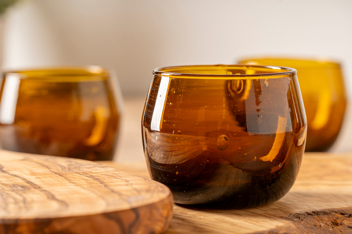 Four amber glass stemless goblets with curved sides arranged on a wooden surface.