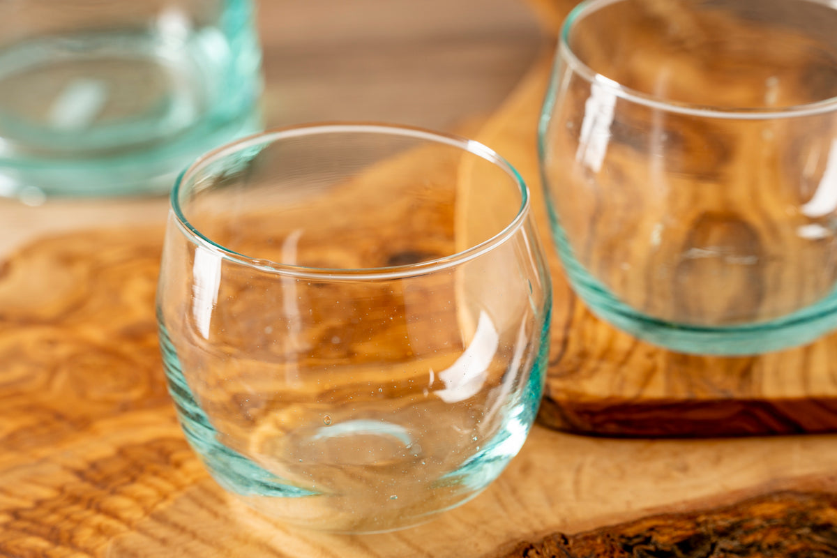 Four clear glass stemless goblets with turquoise-tinted bases on a wooden surface.