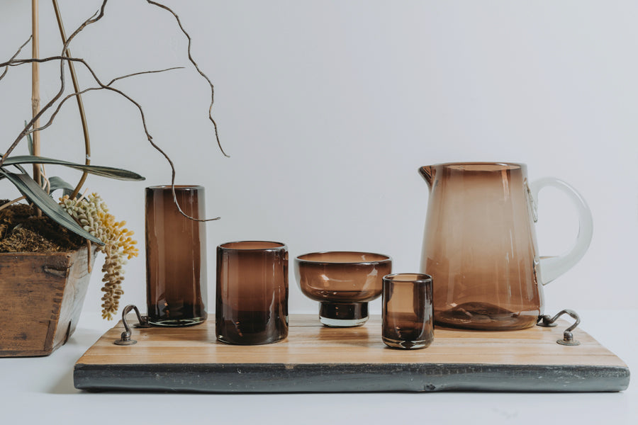 Four handblown shooter glasses in varying sizes with amber-brown glass, displayed on a wooden tray.