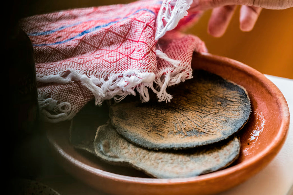 Terracotta ceramic plate holding folded tortillas with a striped cloth napkin.