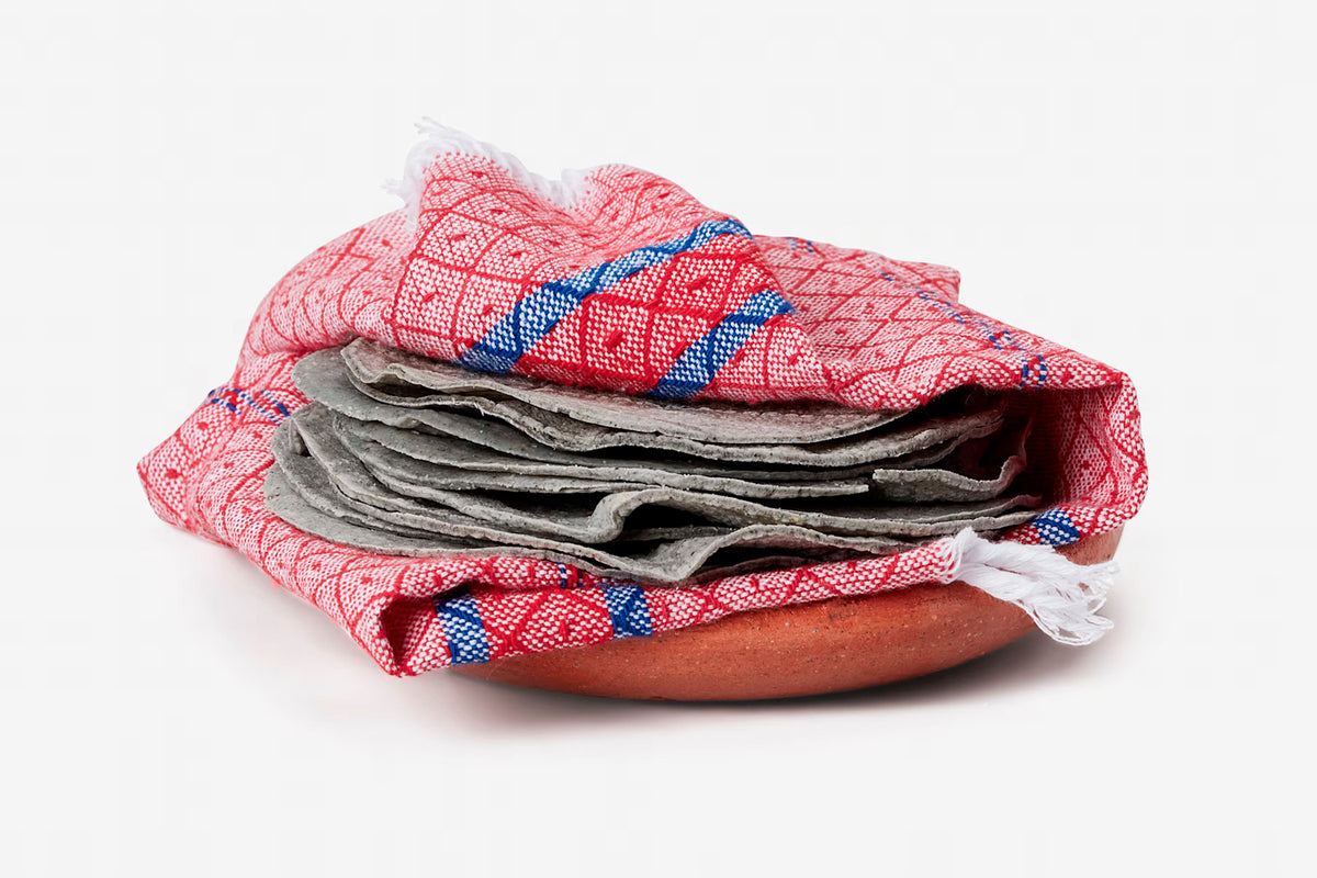 Terracotta ceramic plate partially wrapped in red and blue checkered cloth with gray linens stacked on top.