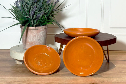 Orange ceramic plate with glazed finish and shallow bowl shape, shown displayed with matching tableware.