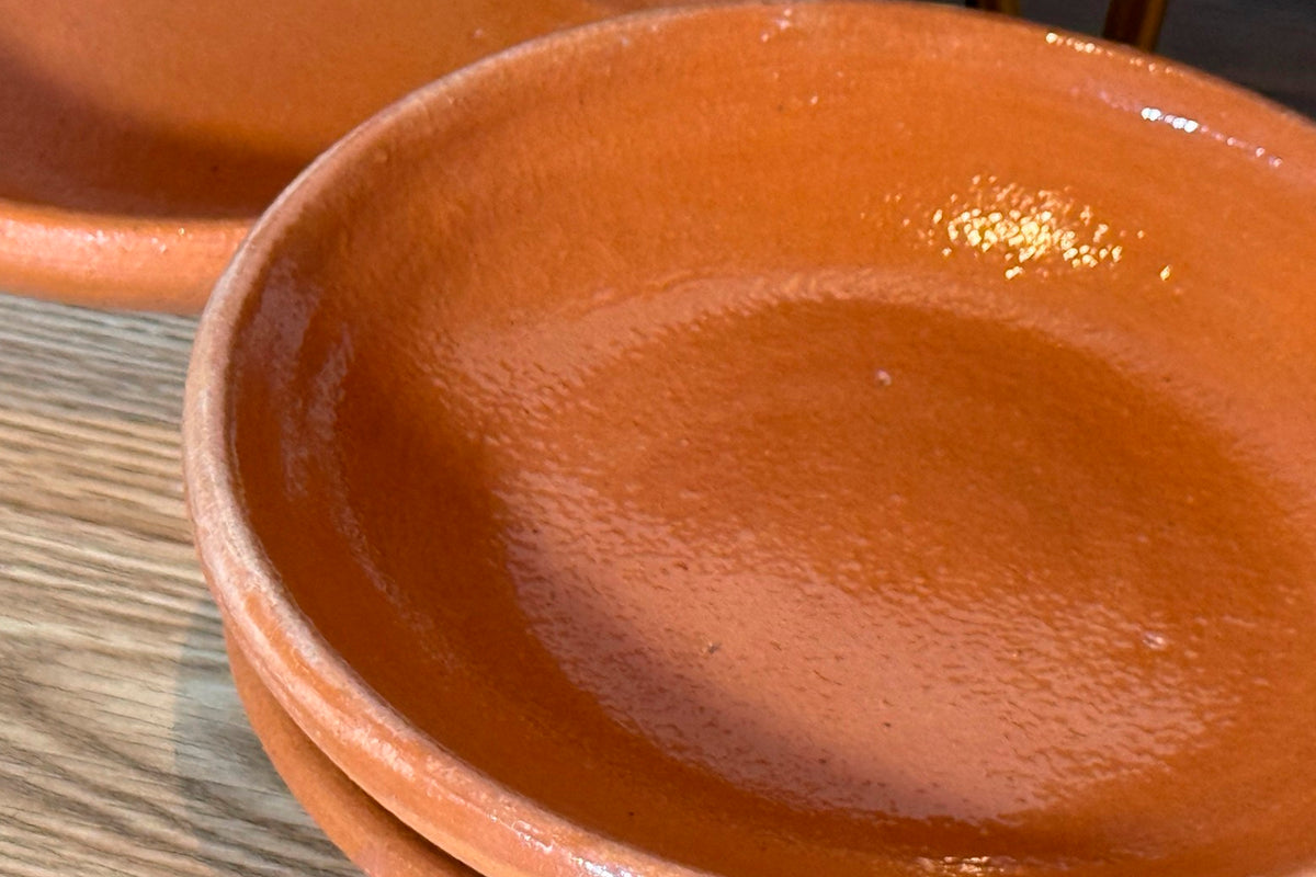 Terra cotta ceramic plate with shallow bowl shape and textured surface finish.