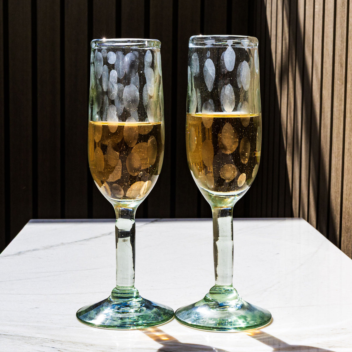 Two clear glass champagne flutes with etched leaf pattern, filled with champagne.