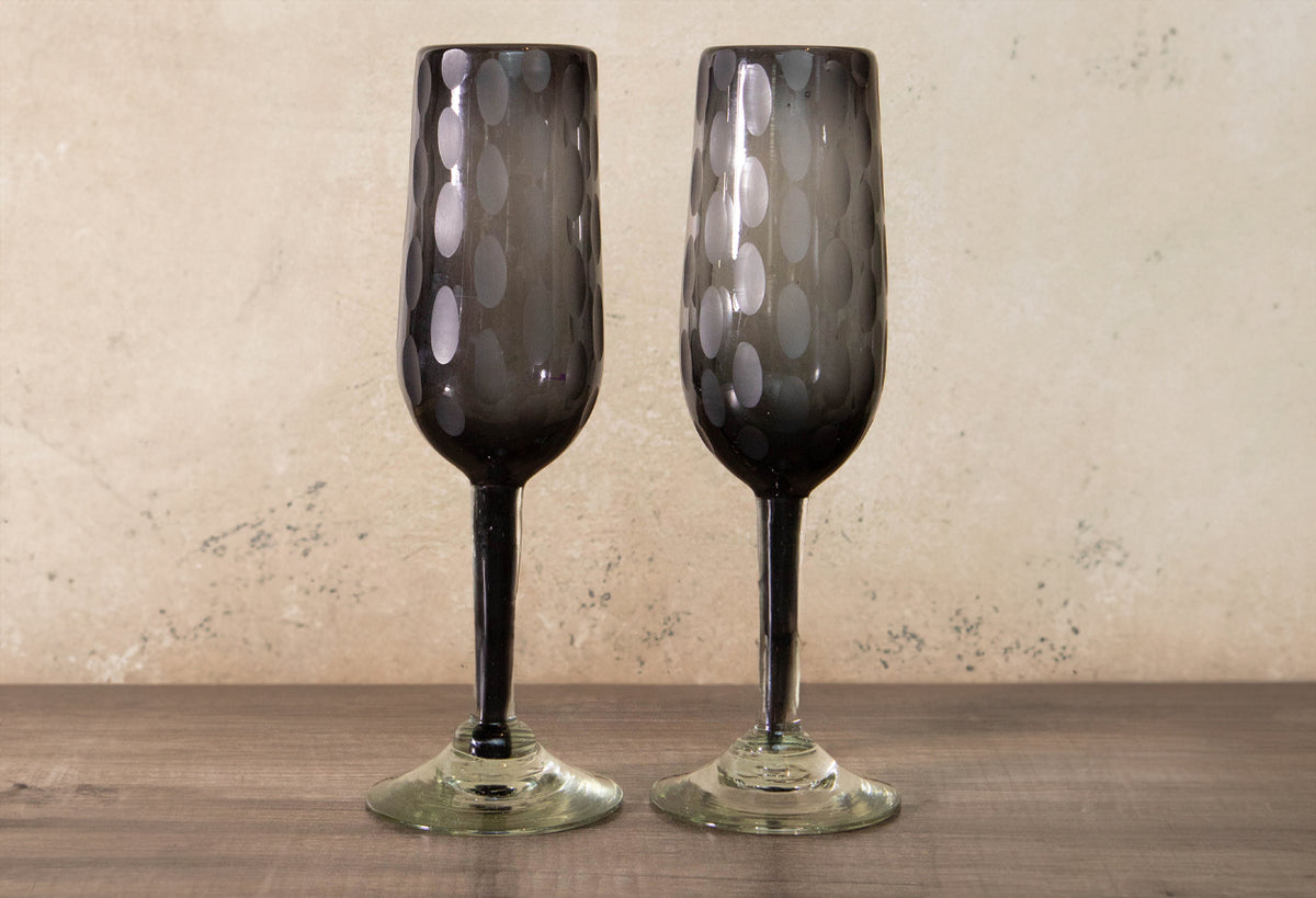 Two dark gray champagne flutes with etched oval patterns and clear glass stems.
