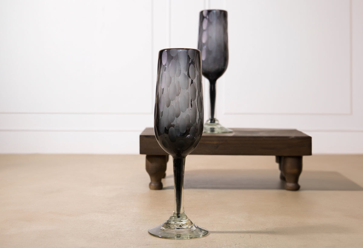 Two smoky gray champagne glasses with etched texture and clear stems, displayed on a wooden stand.