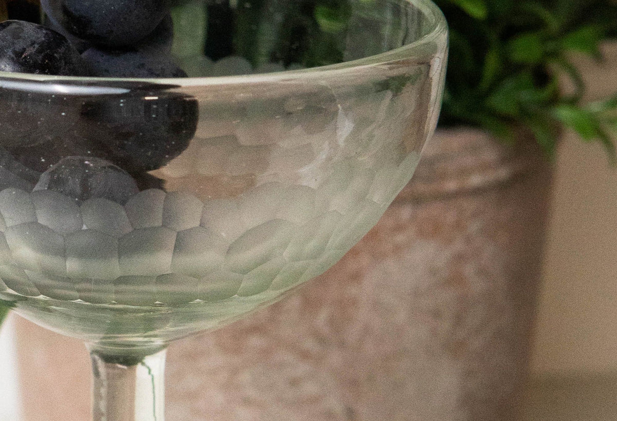 Clear handblown cocktail glass with etched pattern, filled with ice and black olives.
