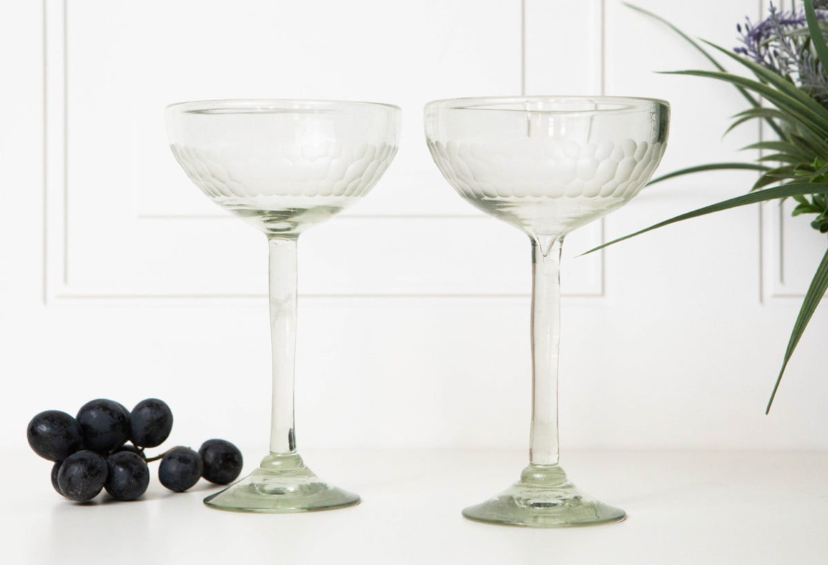 Two clear glass cocktail glasses with etched bowl design and long stems, displayed with grapes and greenery.
