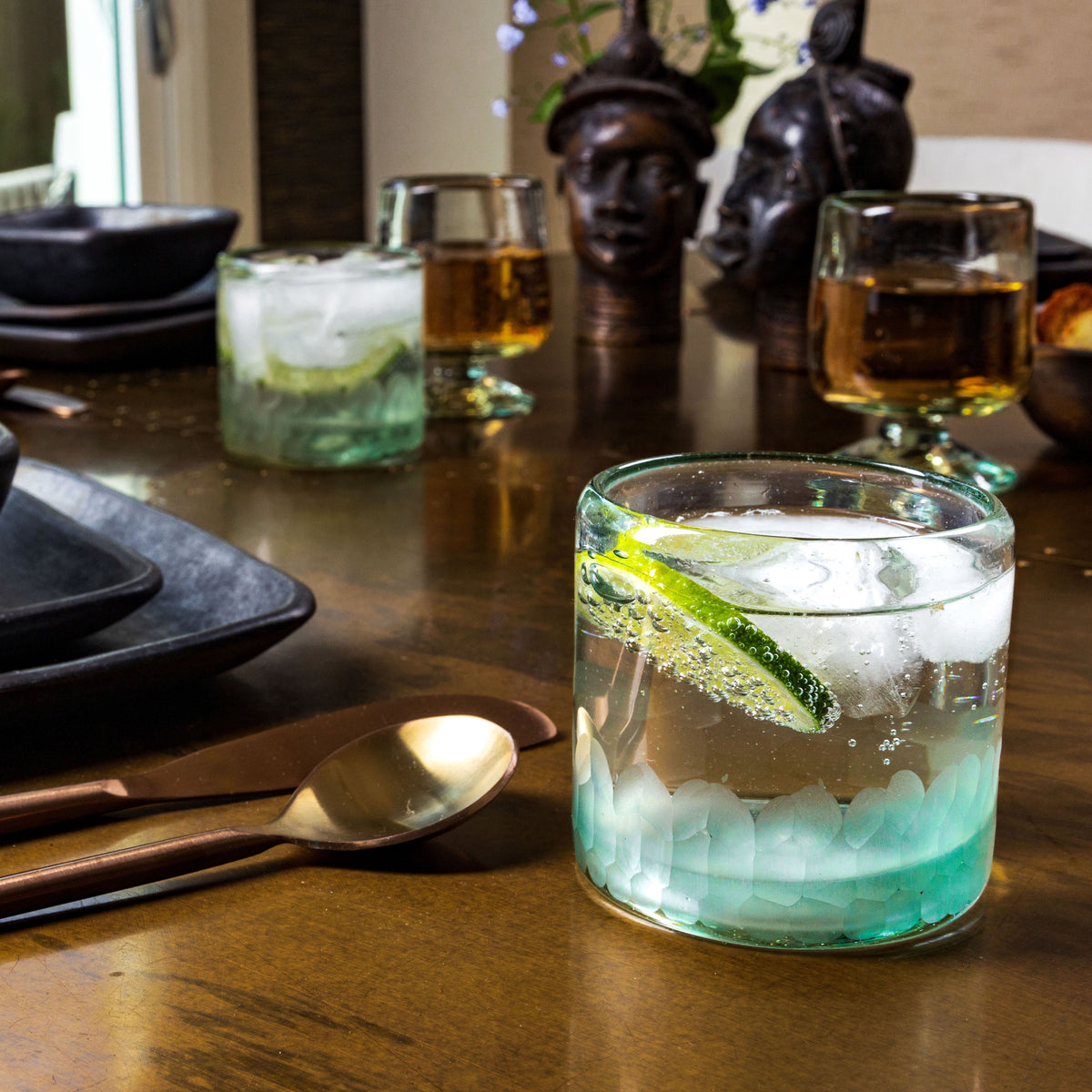 Two handblown rocks glasses with etched texture, one filled with ice and green beverage with lime garnish, displayed on table
