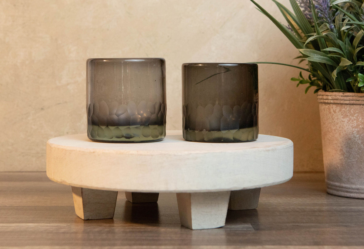 Two smoky gray handblown rocks glasses with etched wavy patterns on a white marble pedestal.
