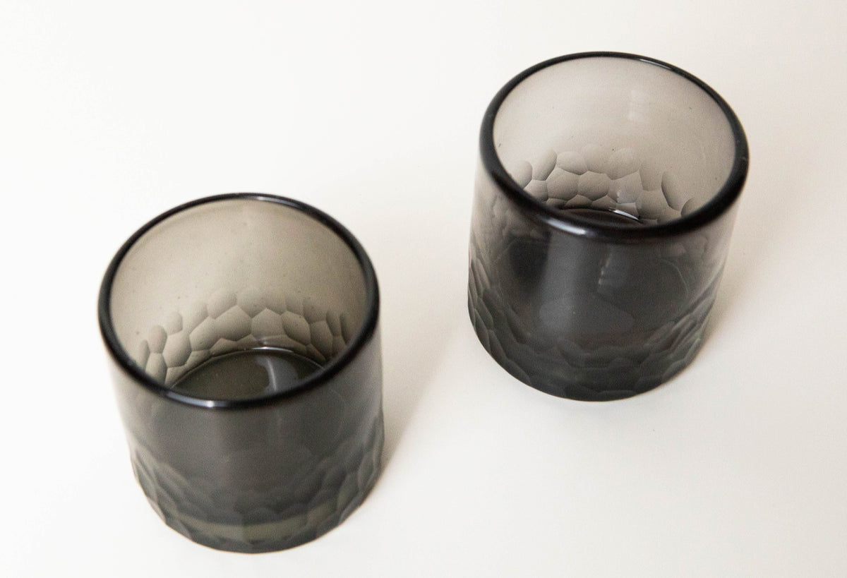 Two smoke-gray rocks glasses with etched leaf pattern and black rim, shown from above.