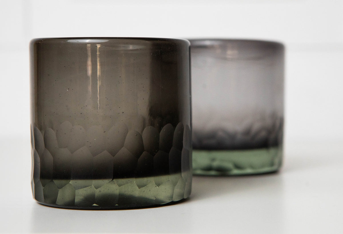 Two smoky gray rocks glasses with etched mountain landscape design and green-tinted base.