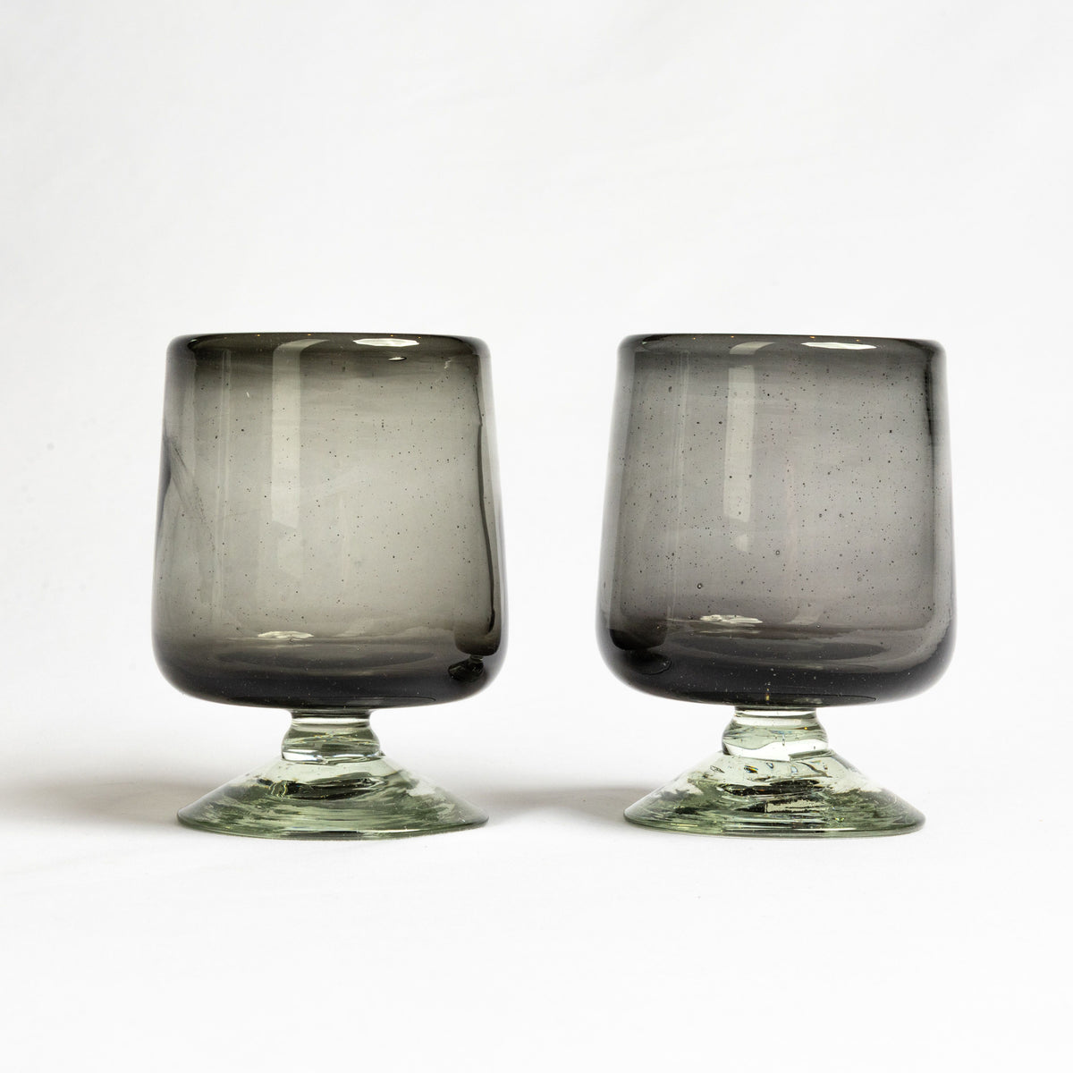 Two smoky gray wine glasses with short green stems and speckled texture throughout the bowls.