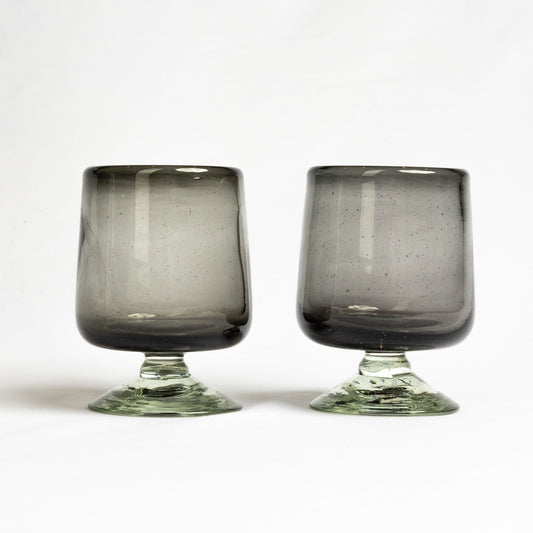 Two smoky gray wine glasses with short green stems and speckled texture throughout the bowls.