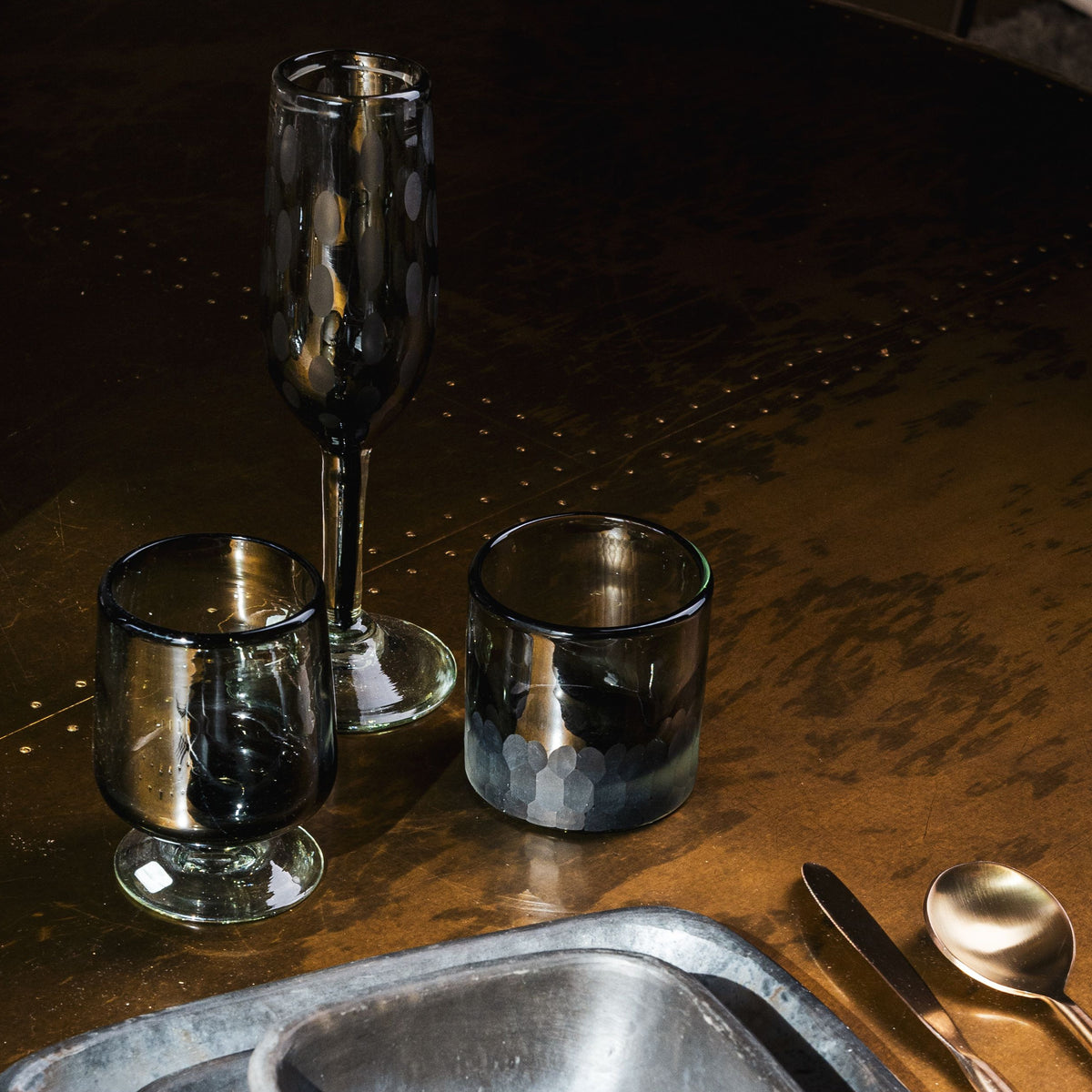 Two clear glass tumblers with short stems and one tall flute glass on a textured bronze surface.
