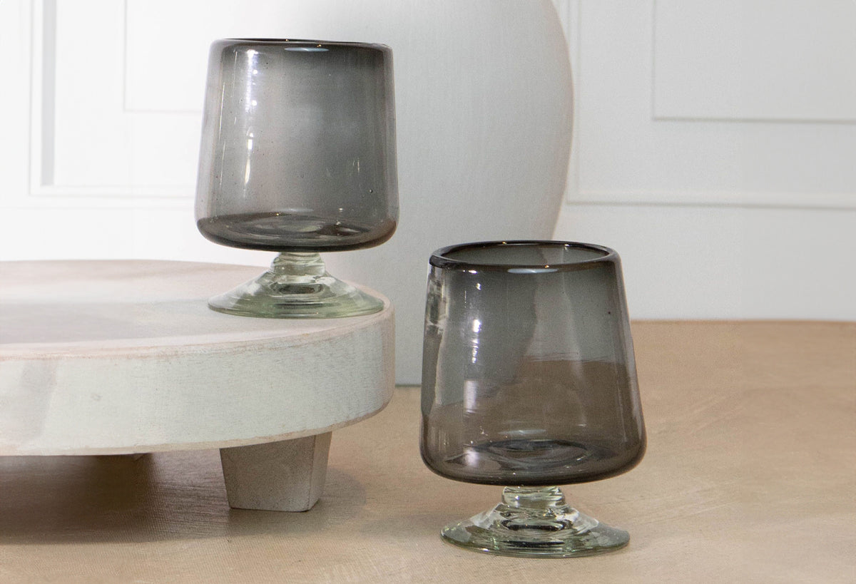 Two short-stemmed wine glasses with smoky gray bowls and clear glass bases.