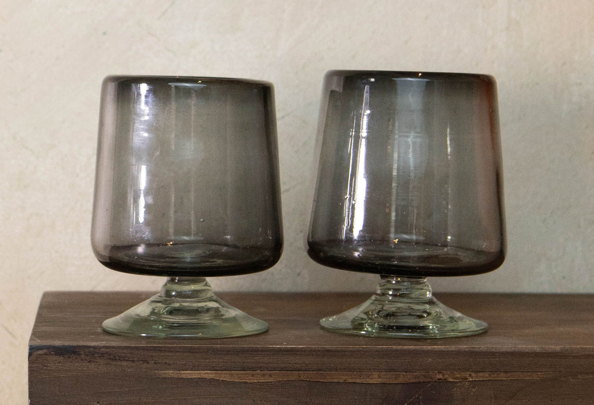Two short-stemmed wine glasses with smoky gray bowls and clear glass bases on a wooden surface.