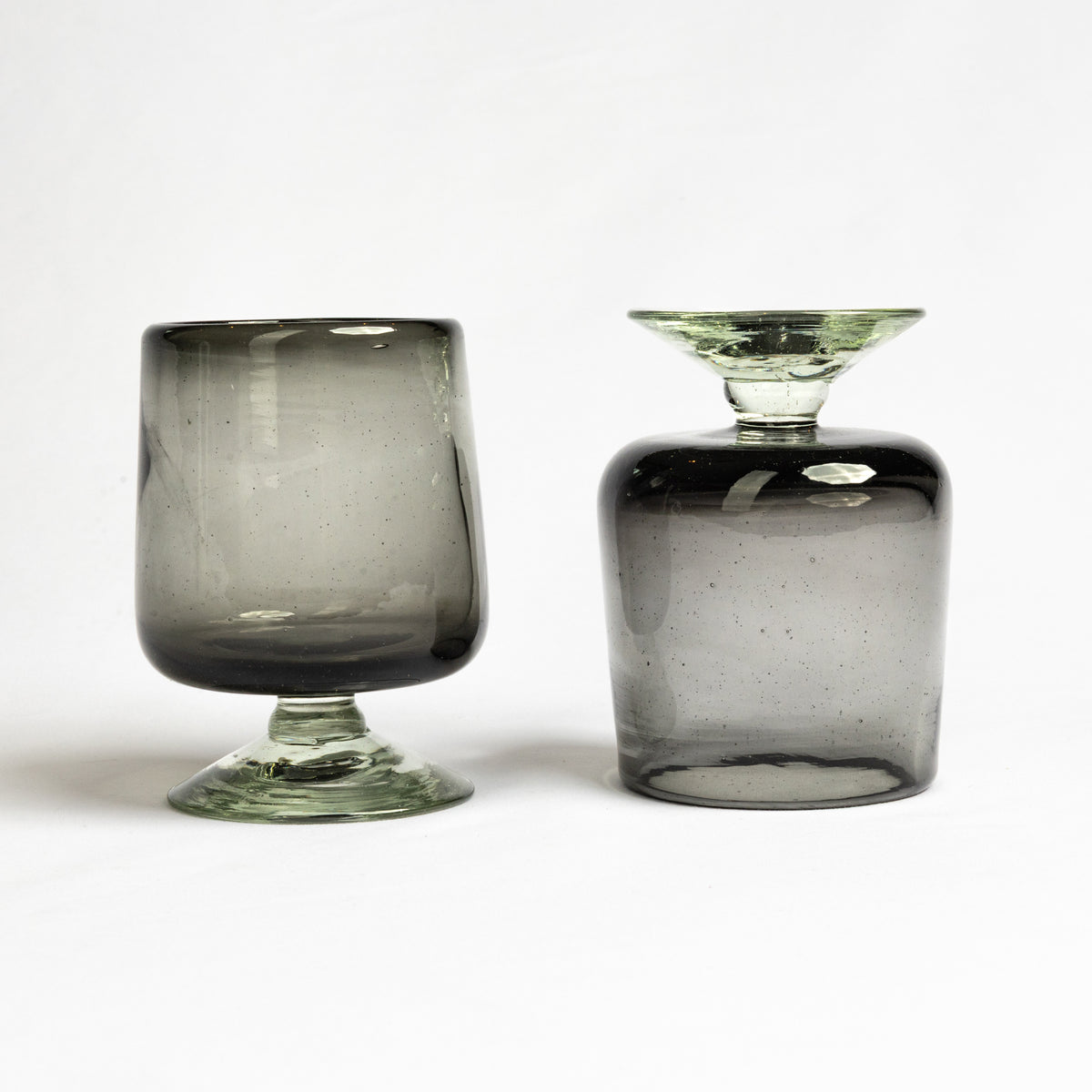 Two gray-tinted wine glasses with short stems and visible bubbles in the handblown glass.
