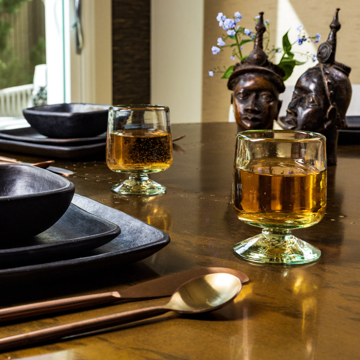 Two clear glass short-stemmed wine glasses filled with amber liquid, displayed on a dining table setting.