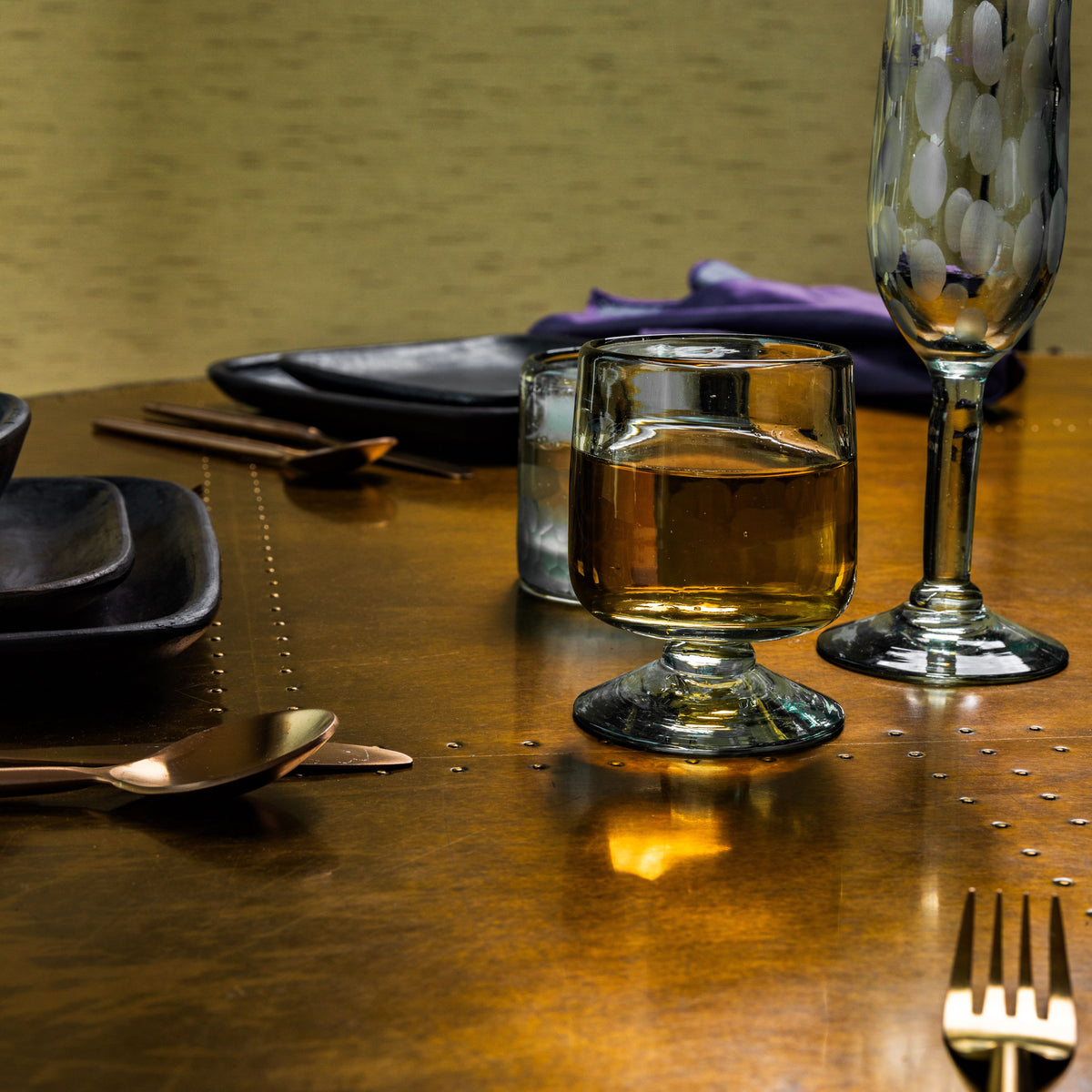 Two clear glass wine glasses with short stems, one filled with amber liquid, on a dining table setting.