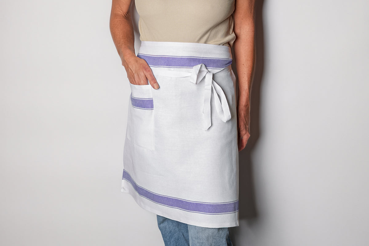 White linen apron with purple stripes, front pocket, and adjustable waist tie worn by man.