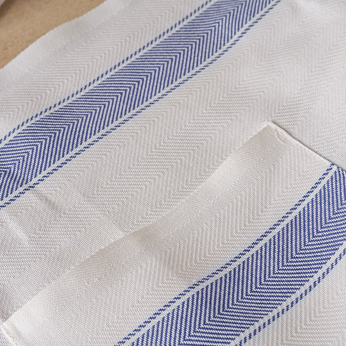 Cream linen apron with navy blue herringbone stripe pattern and woven texture detail.