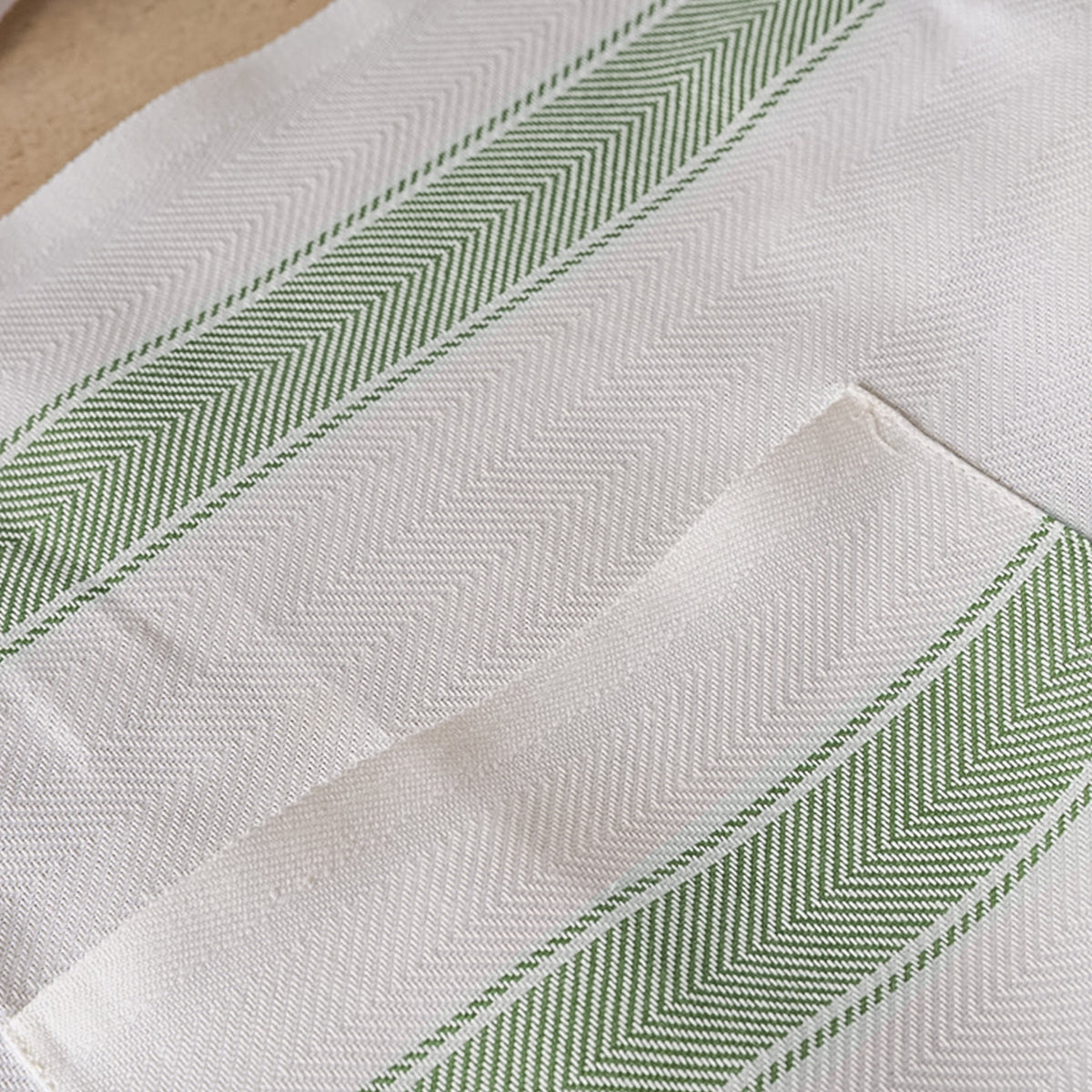 White linen apron with green diagonal striped trim and herringbone weave pattern.