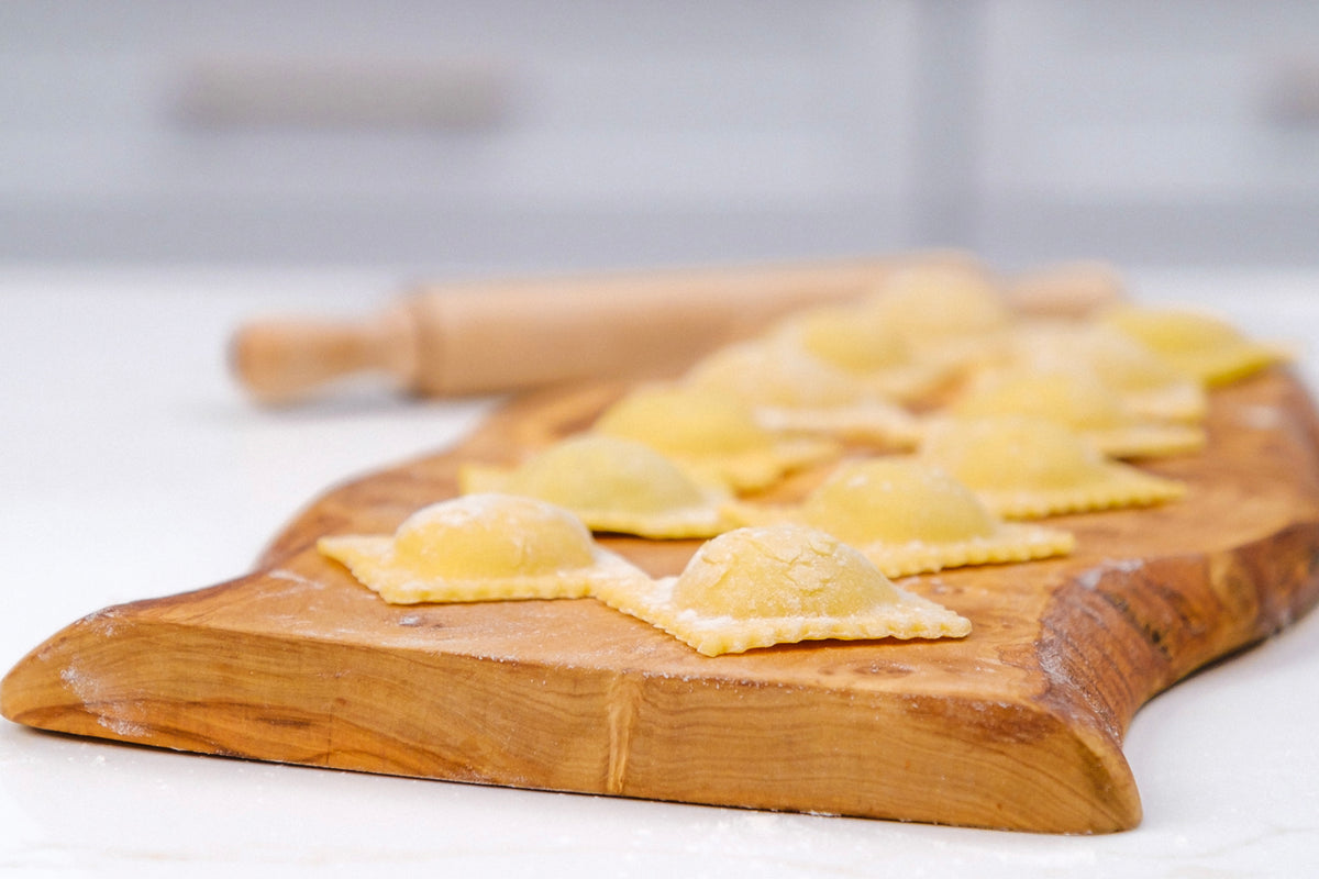 Uncooked pasta shapes arranged on a wooden cutting board with a rolling pin in the background.