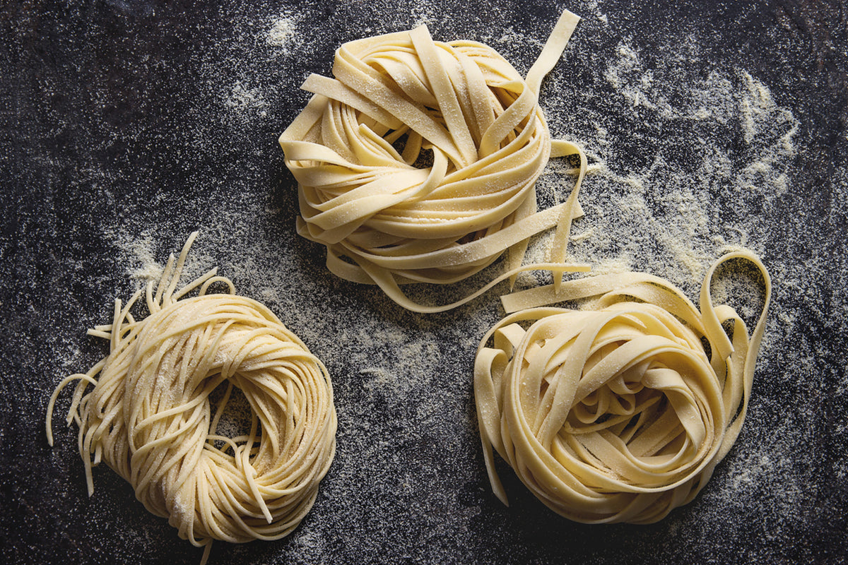 Three bundles of dried pasta nests on dark surface dusted with flour.